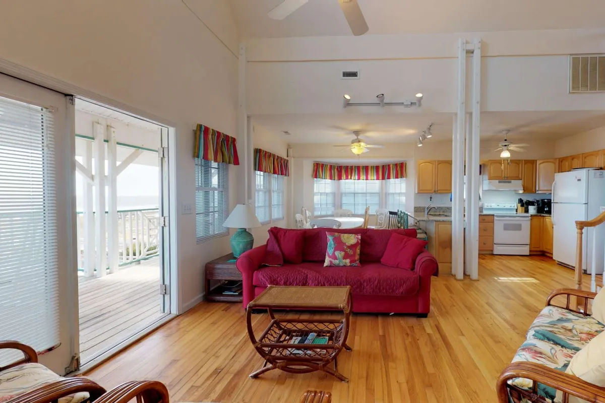 An open-plan interior combining a red sofa, colorful window treatments, a wooden dining table, and an open kitchen area—perfect for relaxed family gatherings and easy entertaining.