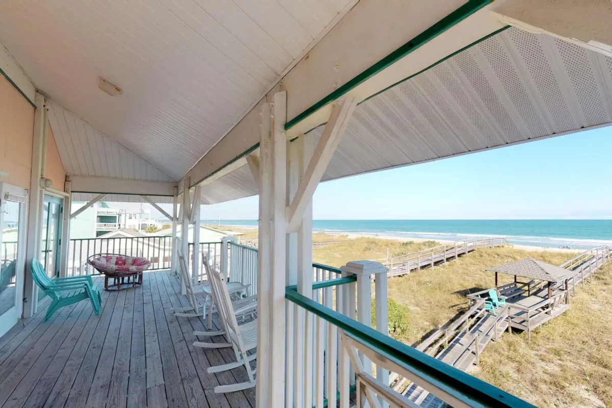 This exterior image captures a wooden deck outfitted with comfortable rocking chairs and an outdoor seating area, all oriented toward a stunning ocean view. The tranquil mood is enhanced by the soft lighting, ideal for sunrise coffees or sunset relaxation.