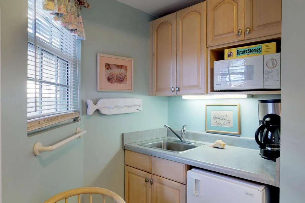 This image features a homey kitchen area with a sink, microwave, and a coffee maker placed near a window with framed artwork. The casual, inviting atmosphere and practical appliances are the focal points.