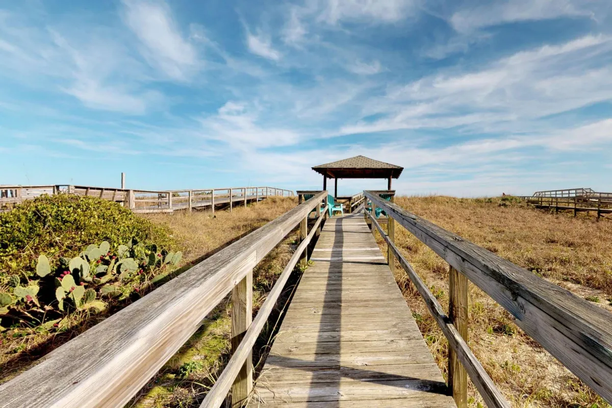 A peaceful exterior scene featuring a wooden pathway leading to a gazebo nestled in lush vegetation. The area invites exploration, quiet relaxation, and offers a sheltered spot for enjoying coastal sunsets or morning coffee.