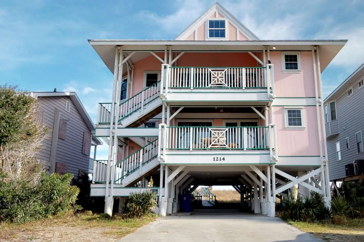 A cheerful view of the pink exterior with white railings and a staircase, setting the scene for family gatherings and outdoor relaxation. The balcony offers space for sunset dinners, morning coffee, and barbecues, all while enjoying glimpses of the ocean.