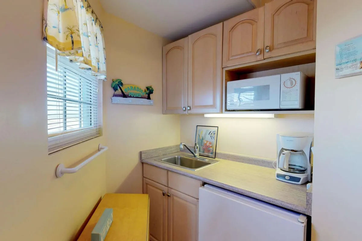 A compact yet well-equipped kitchenette featuring a sink, microwave, coffee maker, and decorative shelving. Warm lighting and thoughtful decor give the space a homey, functional feel, ideal for preparing snacks or a casual breakfast.