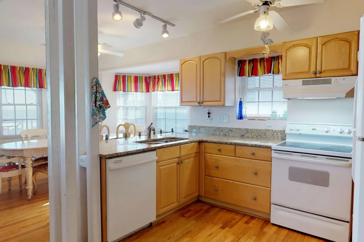 A fully-equipped kitchen with granite countertops, wooden cabinets, colorful window treatments, and modern appliances. The room is warm and welcoming, ideal for cooking group meals or sharing recipes together.