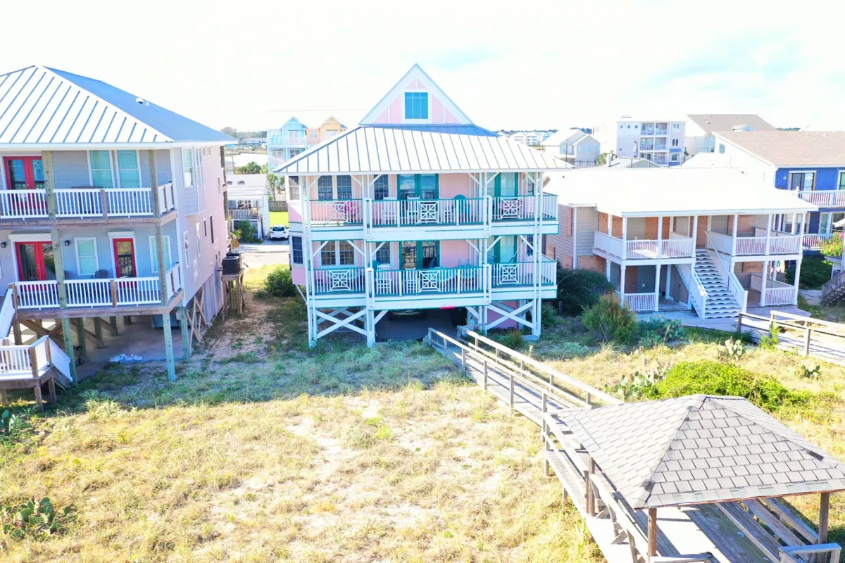 An inviting exterior shot featuring colorful beach houses, a wooden walkway, and a deck area perfect for outdoor dining, barbecues, and taking in memorable sunsets as a group.