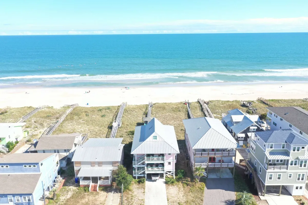 A sweeping view of Carolina Beach’s North End with beachfront houses, sand dunes, and a sandy path leading directly to the ocean. The tranquil seascape captures the proximity of the shore and the ease of beach access for families and groups.